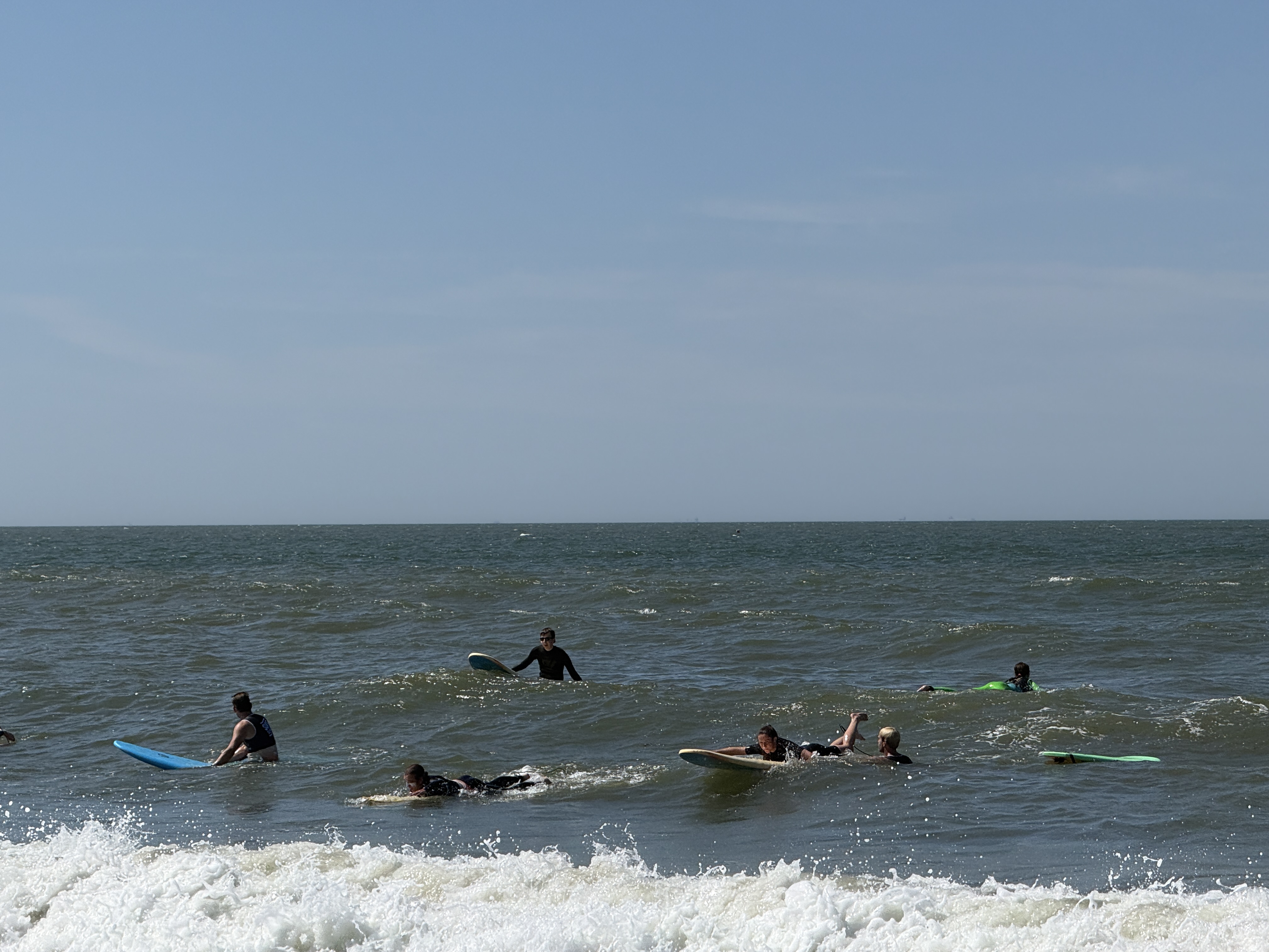Een groep deelnemers en begeleiders staat met Ride the Wave-kleding op het strand.