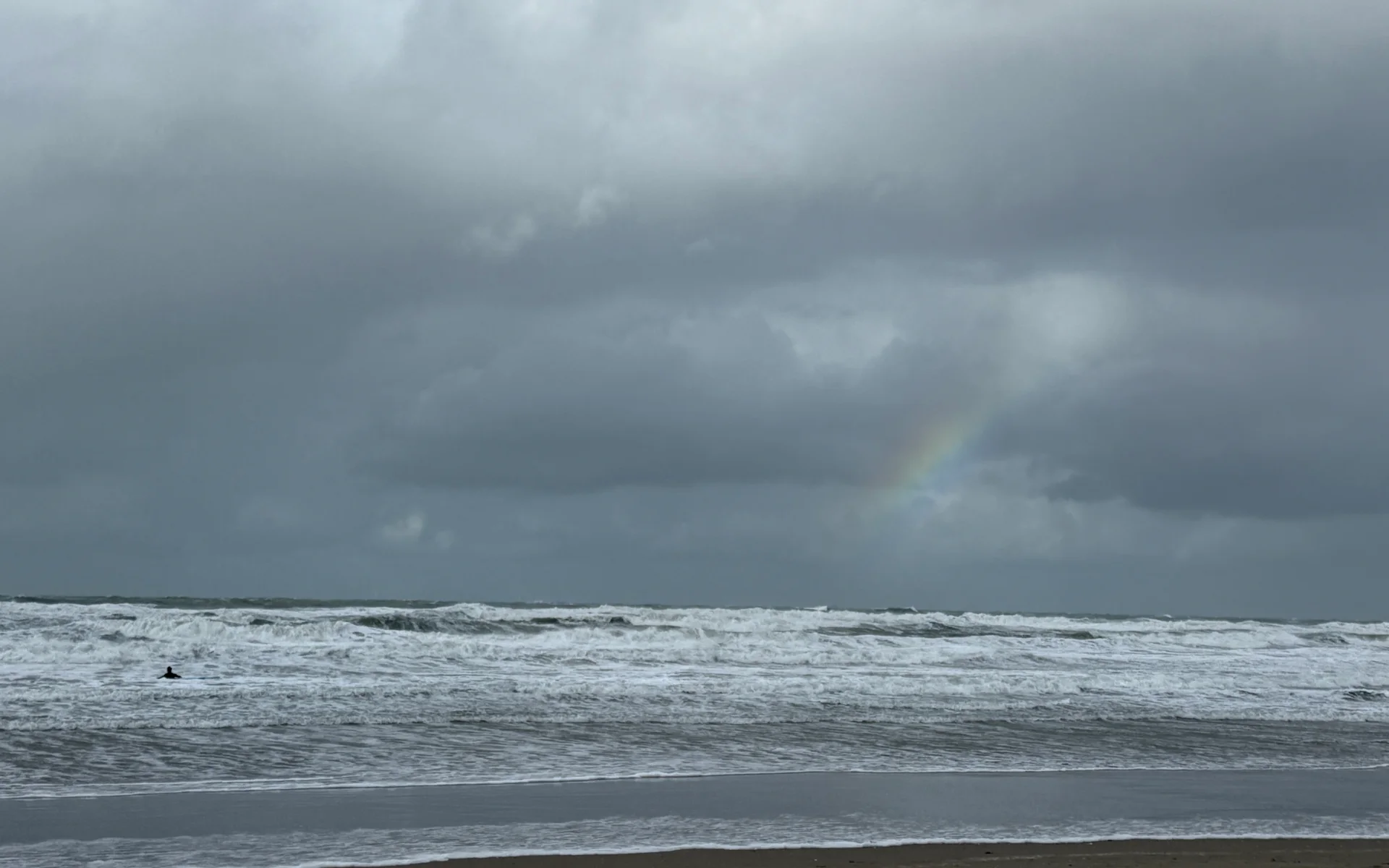 Een stormachtige Nederlandse Noordzee met hoge golven en een regenboog boven het water.