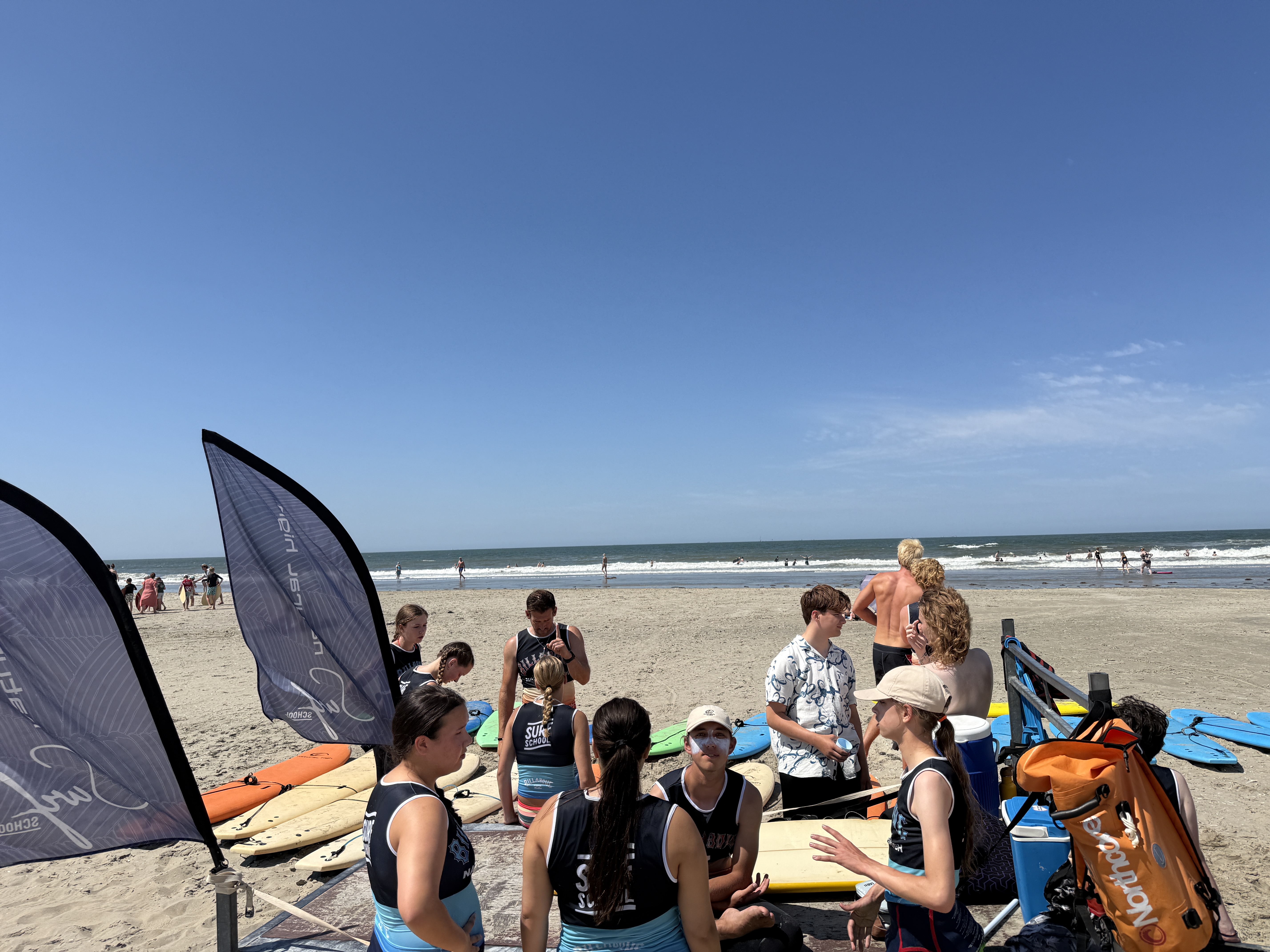 Twee jonge deelnemers in wetsuits staan samen op het strand.