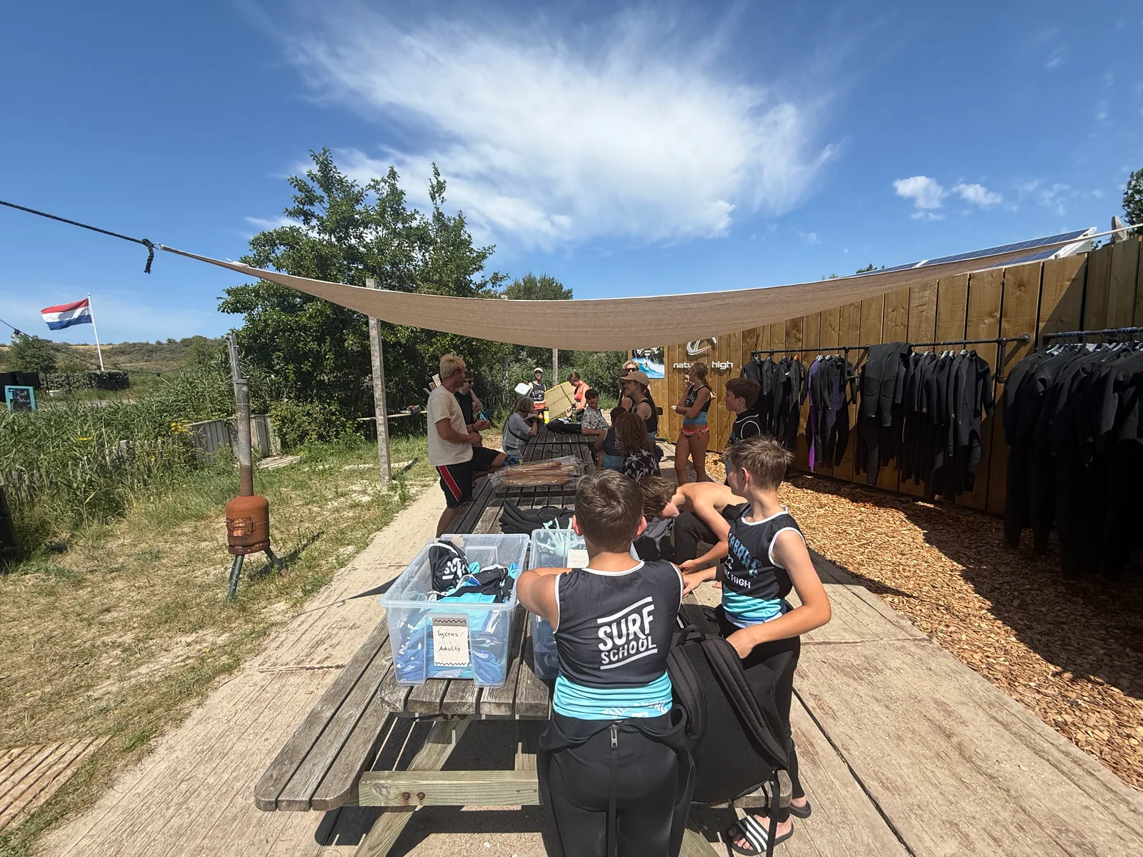 Een groep jongeren en coaches maakt zich klaar bij een rij wetsuits.
